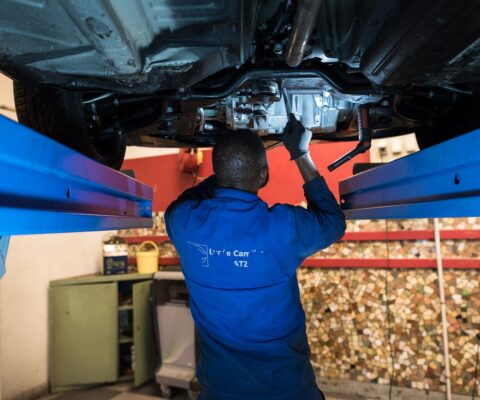 Stagiaire en formation mécanicien automobile travaillant sur une voiture positionnée sur un pont élévateur.